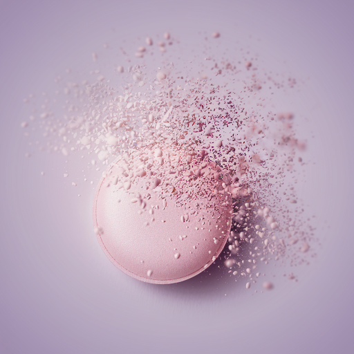 A pink tablet dissolving into fine particles, set against a soft lavender background.