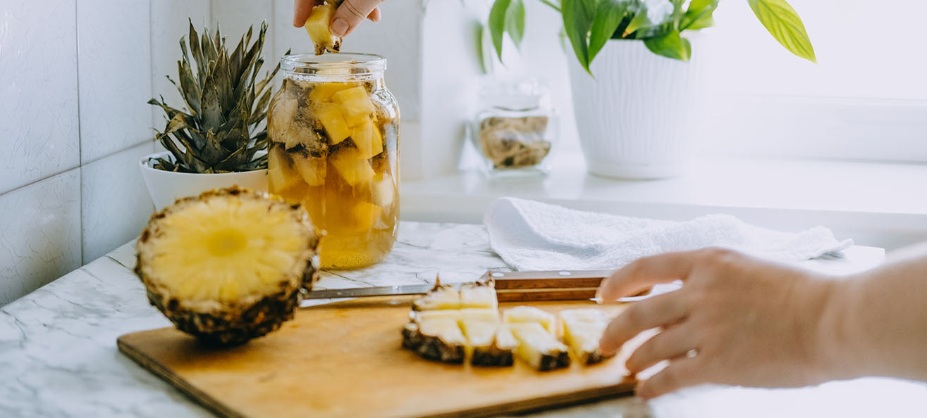 Person cutting pineapple and adding to a glass for fermented drink