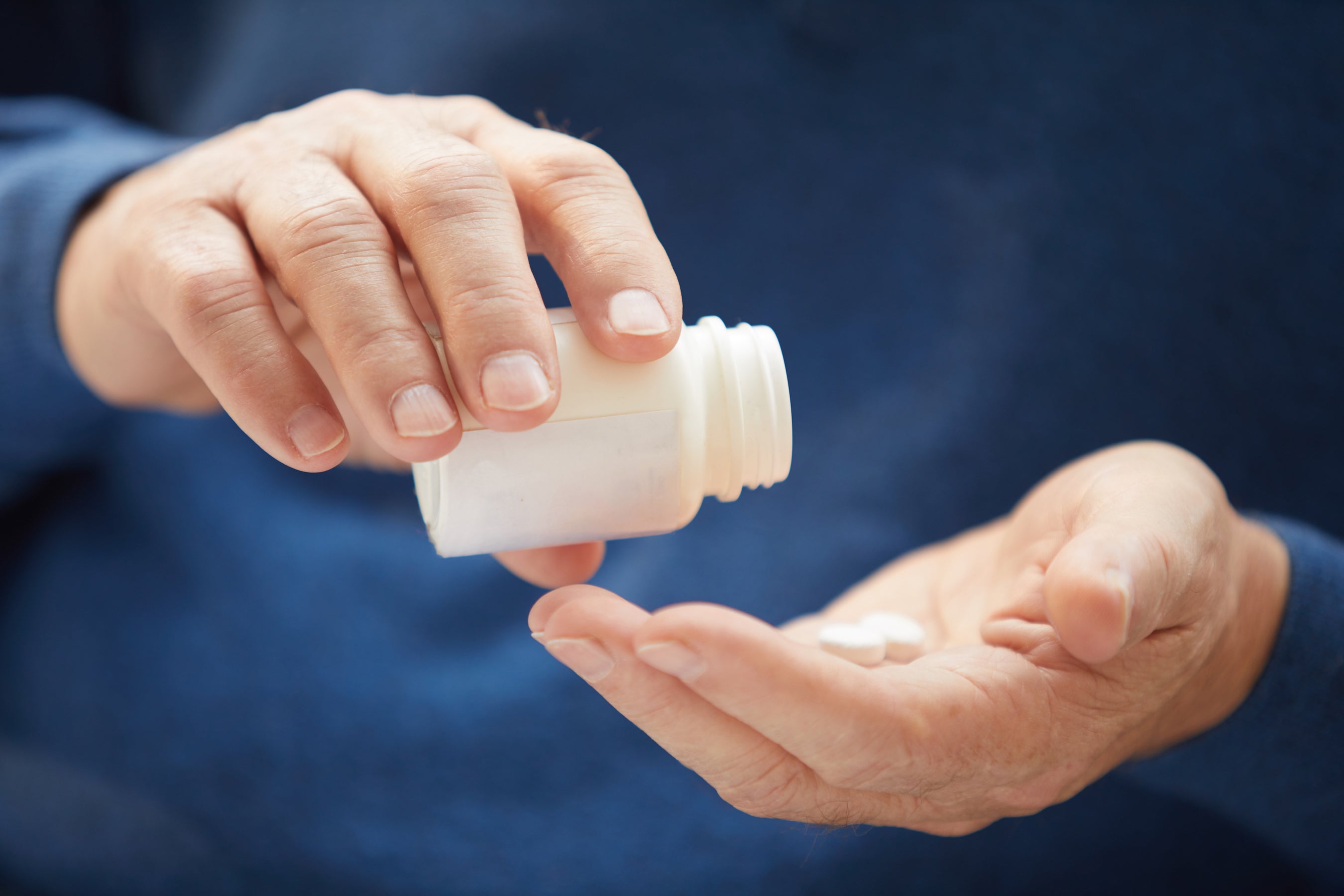 Person holding a bottle and two pills on palm of his hand